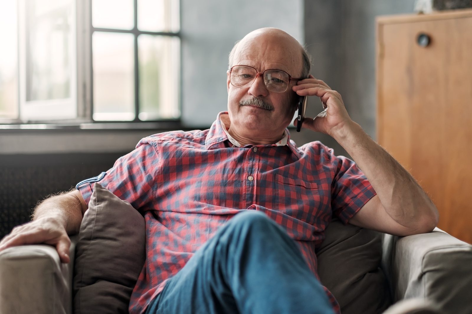 An older man at home, smiling, on the phone - the kind of resident a council adult social care team calls on a care technology check-in