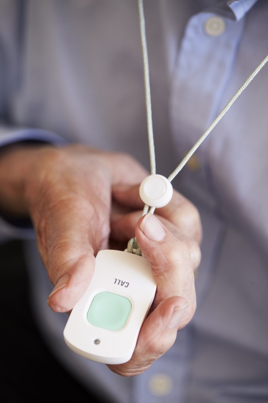 Close-up of a hand holding a personal alarm pendant with a green CALL button on a lanyard - typical council-issued care technology
